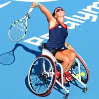 Female wheelchair tennis player with arm raised over head hitting a ball